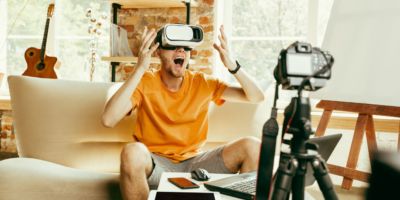 Full of emotions. Caucasian male blogger with professional camera recording video review of VR glasses at home. Blogging, videoblog, vlogging. Man using virtual reality headset while streaming live.