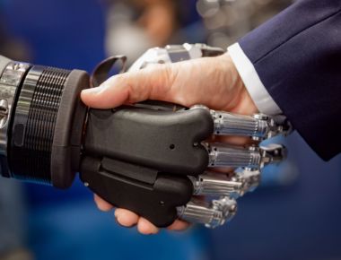 Hand of a businessman shaking hands with a Android robot. The concept of human interaction with artificial intelligence.
